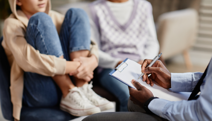 Close up of African-American psychologist taking notes on clipboard in therapy session for children.