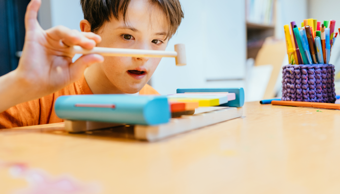 Close up of cute kid with special needs playing with developing musical toys while sitting at the desk in daycare center.