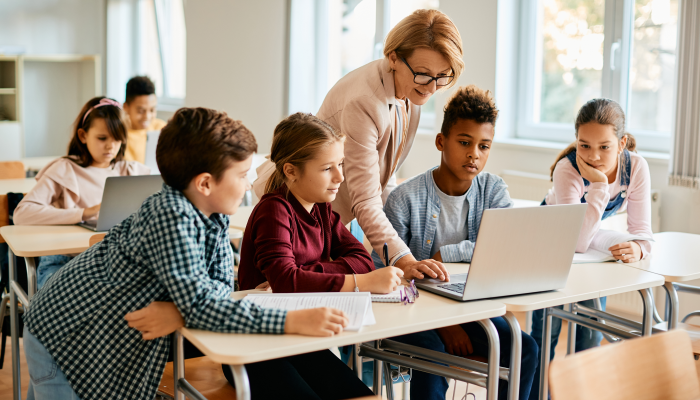 Elementary teacher and her students using laptop during computer class at school.