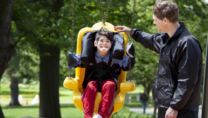 Father pushing disabled boy in special needs handicap swing.