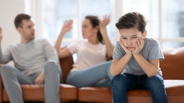 Frustrated little school boy feeling depressed while angry parents fighting at home.