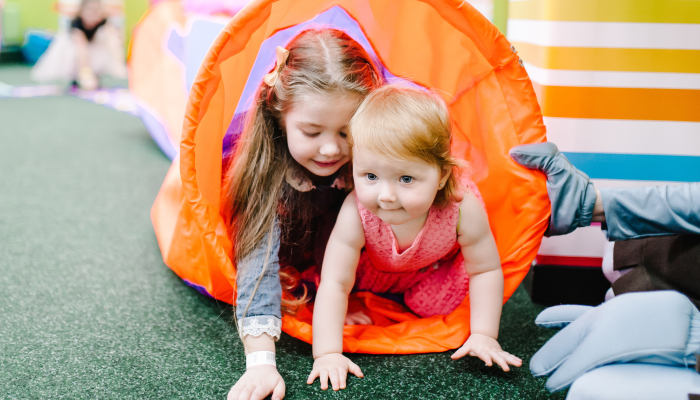 Happy children, baby little girls running in the tunnel and playing toys in children's play room on her birthday.