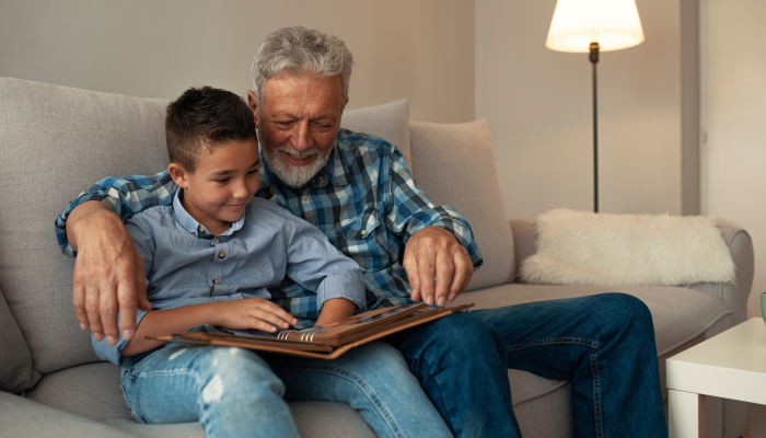 Happy family elderly man and little boy smiling r while sitting on couch and reading fascinating fairy tale together at home.