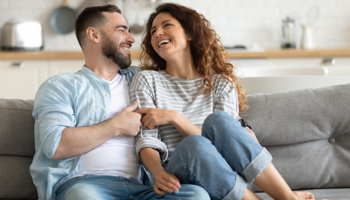 Happy married young couple hugging, sitting on cozy couch together.