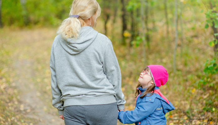 Mother and little girl with special needs walks at autumn park.