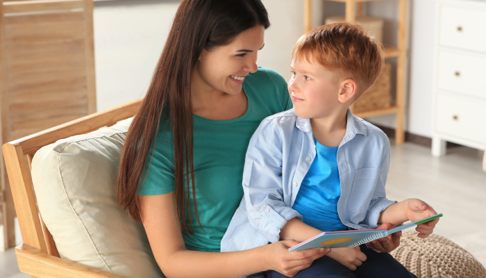 Mother reading book with her son on armchair in living room at home.