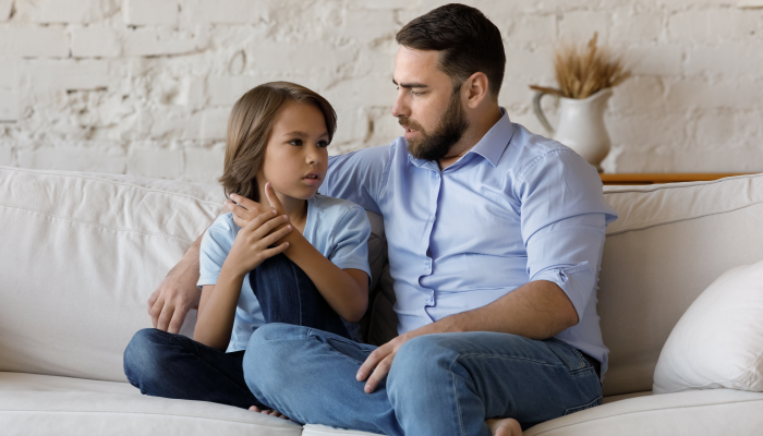 Serious father listen to his pre-teen little son talking seated on sofa at home.