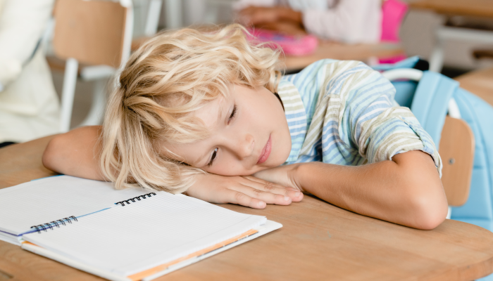 Sleepy tired bored schoolboy pupil student sleeping at the desk in school during the lesson class.