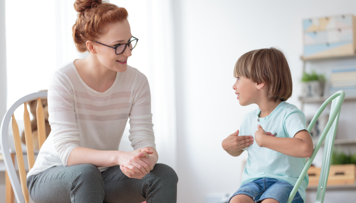 Smiling little boy talking with cheerful child psychotherapist during therapy session at office.