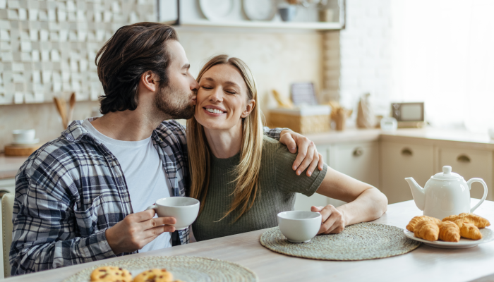 Smiling millennial caucasian husband with stubble hugs and kisses his wife on cheek.