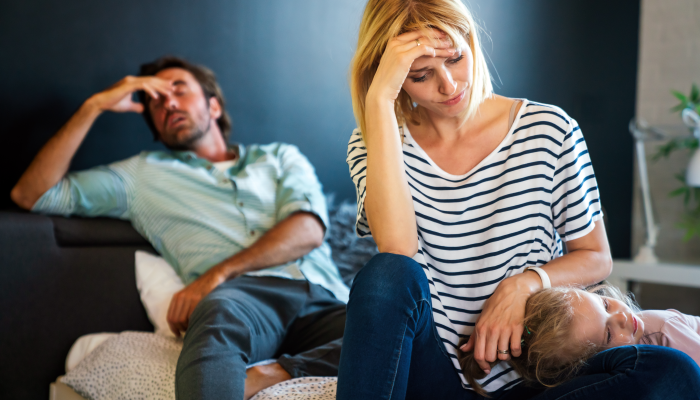 Tired mother and father sitting on couch feels annoyed exhausted stressful with little girl child.