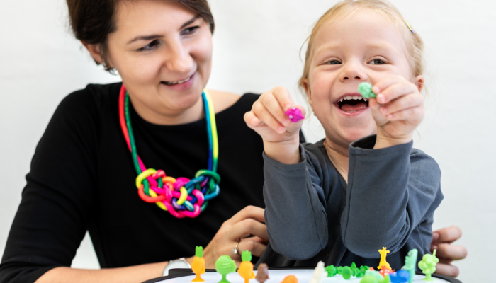 Toddler girl in child occupational therapy session doing sensory playful exercises with her therapist.