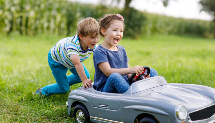 Two happy children playing with big old toy car in summer garden, outdoors.