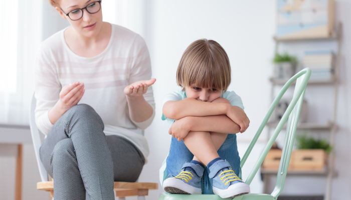 Worried autistic boy sitting with crossed legs on mint chair during conversation with psychiatrist.