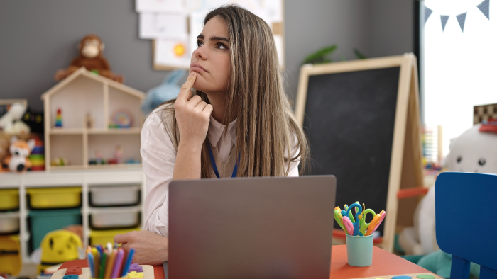 Young beautiful hispanic woman preschool teacher using laptop thinking at kindergarten.