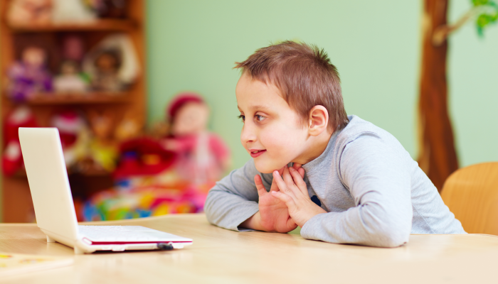 Young boy with special needs watching media through the laptop.