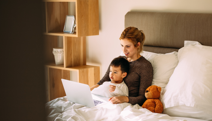 Young mother with her beloved son in the bedroom on the bed watching a movie on laptop.