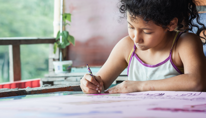Close-up of a brown-skinned latina girl, coloring her homework with a purple pencil.
