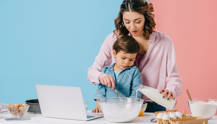 cute little boy looking at laptop display while mother cracking walnut on bicolor background.