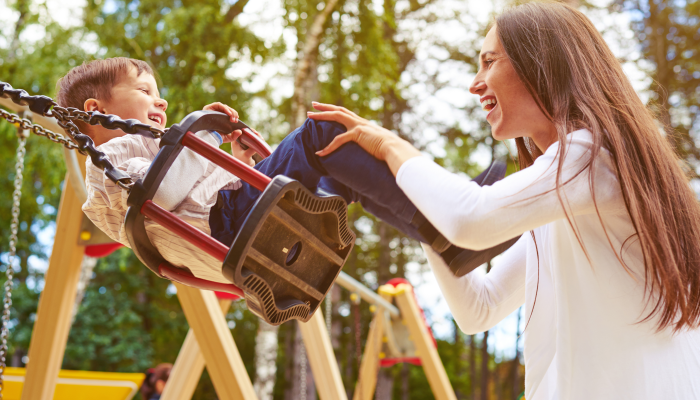 Happy mother pushing laughing son on swing in a park.