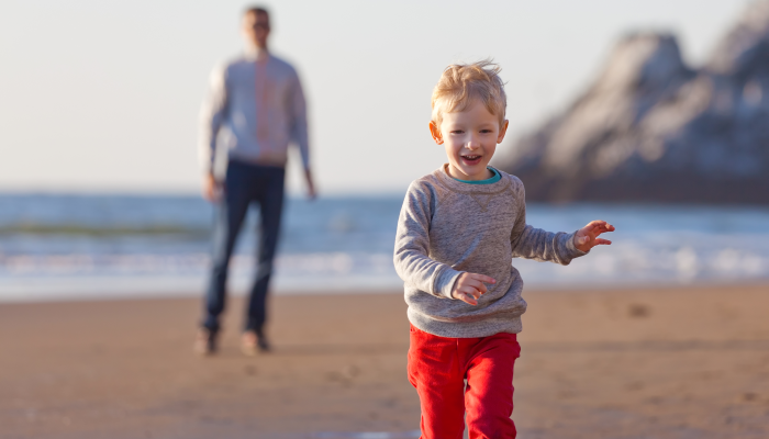 Happy smiling boy running away from his father at the beach in california.