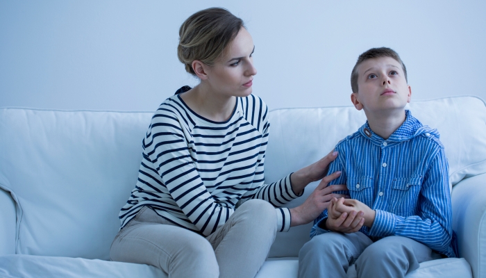 Autistic boy sitting on a sofa with his carer trying to calm him down.