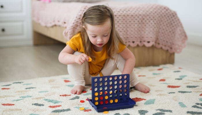 Charming Caucasian girl blonde 4 years old with Down syndrome plays with educational game in the nursery on the floor.