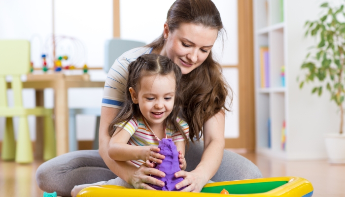 Child girl and woman mould with kinetic sand in playschool or daycare.