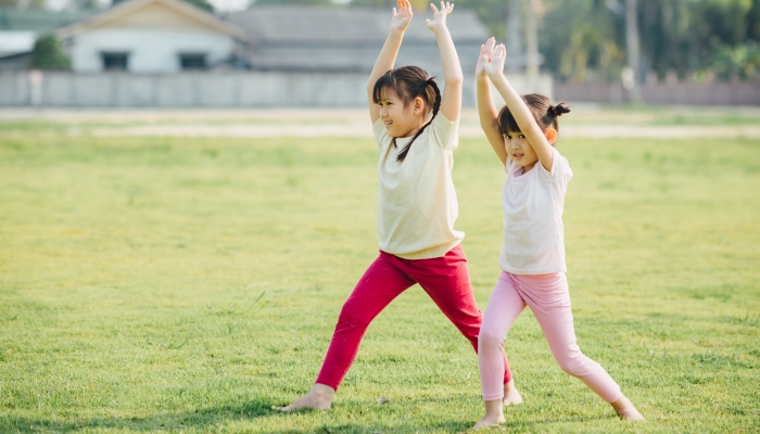 Children meditation with yoga pose on green grass field.
