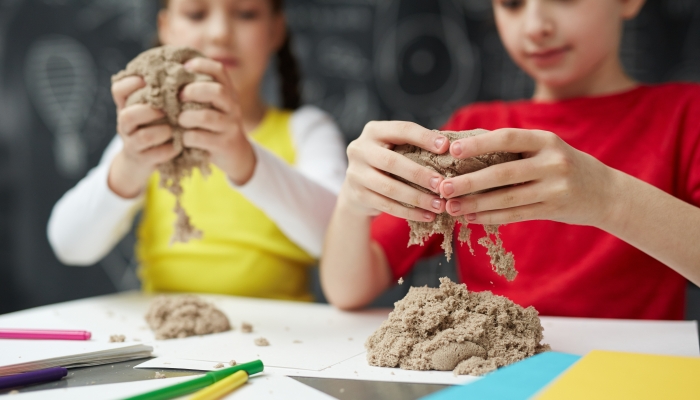 Creative girls making figures from kinetic sand at lesson.