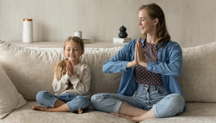 Happy mom and peaceful little daughter kid meditating at home together.