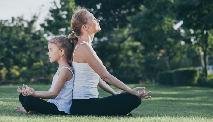 Mother and daughter doing yoga exercises on grass in the park at the day time.