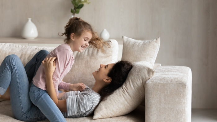 Smiling young Hispanic mom and small ethnic daughter relax on sofa in living room have fun play together.