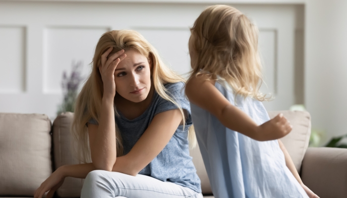 Stressed young woman nanny irritated by loud hyperactive little preschool kid girl at home.