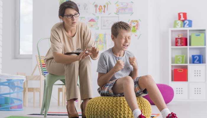 Temper tantrum concept, little angry emotional boy being aggressive during therapy session with child psychotherapist.