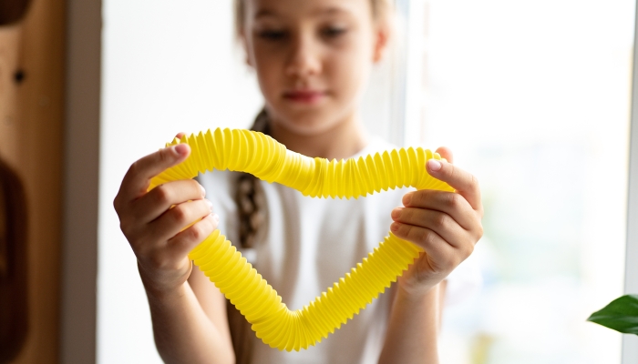 Anti stress sensory pop tube plastic toy in a kid's hands. a little happy child girl plays with a poptube fidget toy at home.