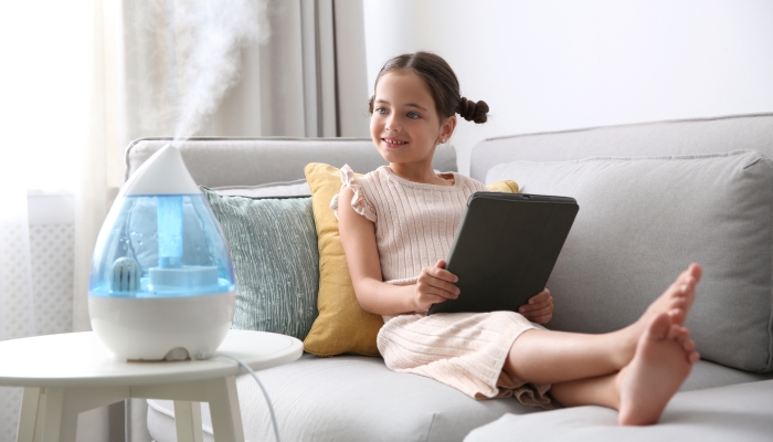 Little girl using tablet in room with modern air humidifier.