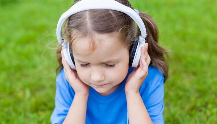 Portrait of a cute child girl listening to music in white headphones in the city outdoors on a summer Sunny day.